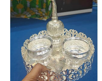 Puede incluir: Una bandeja de plata con diseños intrincados, que incluye dos cuencos pequeños y una botella decorativa con un pico. La bandeja es perfecta para servir o exhibir artículos pequeños.