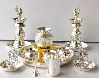 May include: An assortment of silver religious items, including two tall lamps with bird figures, a small vase, several bowls, a cup, and a tray. The items are arranged on a light surface.