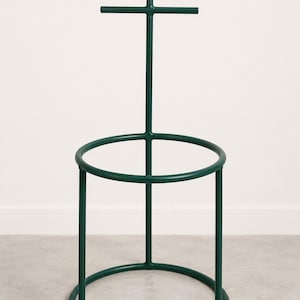 May include: A dark green metal coat rack with a circular base and a vertical pole. Two horizontal bars extend from the pole, and two more extend from the top. The rack is designed to hold coats and other items.