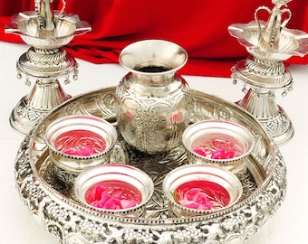 May include: A silver tray with four small bowls filled with pink flower petals, a silver pitcher, and two silver candle holders. The tray has an ornate design and is decorated with floral motifs.
