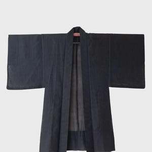 Può includere: Un abito in stile kimono blu navy scuro con maniche larghe, appeso a una gruccia nera. L'abito presenta un design semplice ed elegante con linee verticali e una sottile lucentezza. L'indumento è aperto sul davanti.