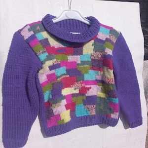 Peut inclure: Pull en maille violet avec un motif patchwork coloré. Le pull a un col montant et des manches longues.