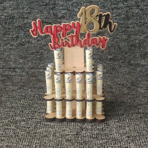 May include: A wooden stand with a tiered design holds rolled up bills. The stand is decorated with the words "Happy 18th Birthday" in red and black lettering.
