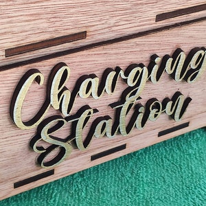 Könnte beinhalten: Eine Holzkiste mit einem Schild, auf dem "Charging Station" in goldenen Buchstaben steht.