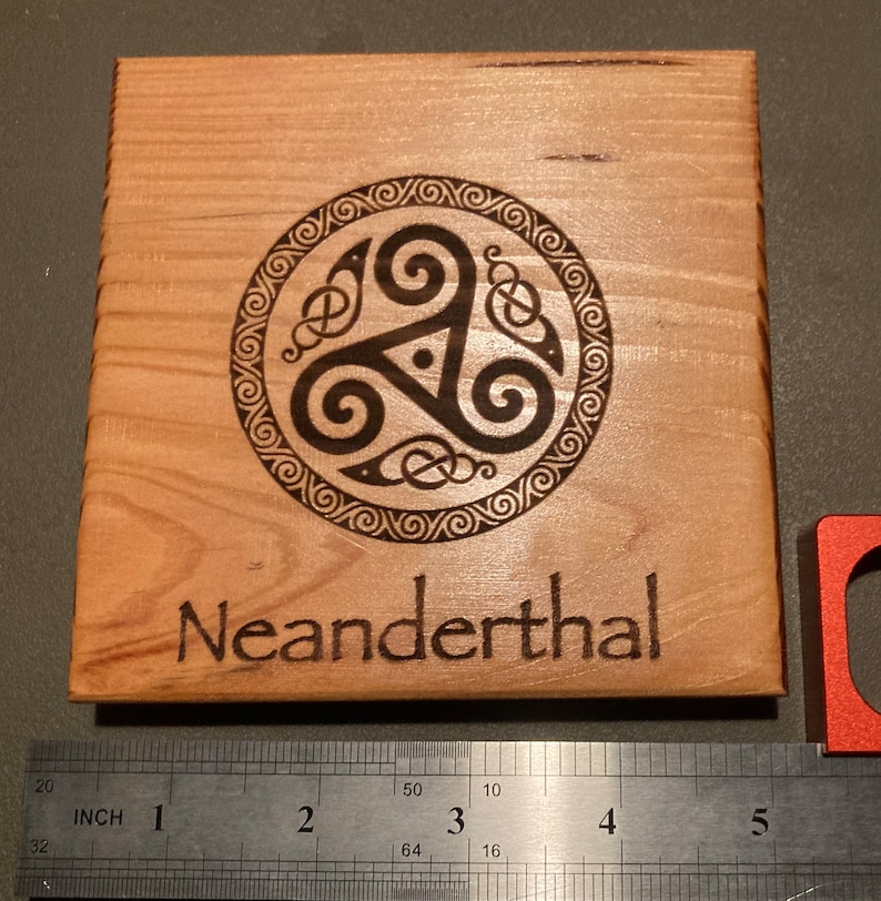 May include: A wooden coaster with a Celtic knot design and the word "Neanderthal" engraved on it.