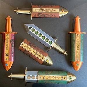 May include: Five different dice holders, each with a unique design and name. The holders are made of leather and metal and feature a variety of colours, including brown, green, red, and gold. The holders are designed to hold dice for role-playing games.