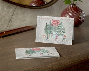 May include: A Christmas card with a snowy forest scene featuring snowmen and the text "Seasons Greetings".