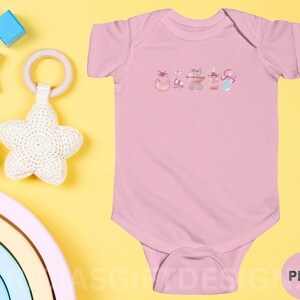 May include: Pink baby onesie with a watercolor design of a baby carriage, a bottle, a pacifier, and a toy. The onesie is on a yellow background with other baby toys.