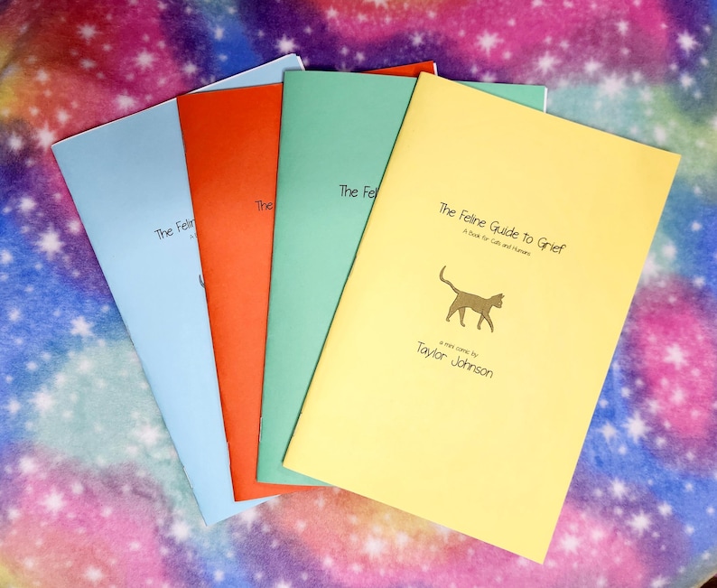 May include: Four books with colorful covers: light blue, orange, green, and yellow. The yellow book is titled "The Feline Guide to Grief" with a cat illustration and author's name. The other books have the title "The Feline..." on the cover.