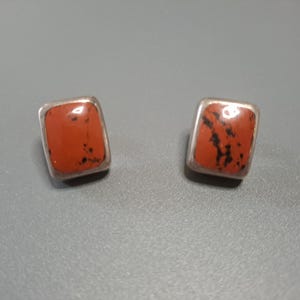 May include: A pair of silver earrings with square red and black stone settings.