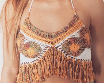 Peut inclure: Un haut de bikini crochet blanc avec une bordure en franges. Le haut présente un motif floral avec des accents bruns, orange et verts.