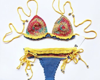 May include: A crocheted bikini set with a tie-dye pattern in shades of red, yellow, blue, and green. The top is a triangle style with yellow ties and the bottom is a high-waisted style with yellow ties on the sides.