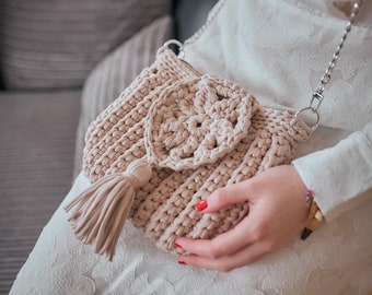 May include: A crocheted beige bag with a large crocheted flower design and a tassel. The bag has a silver chain strap.