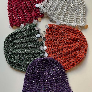 May include: Five crocheted hats in various colors: red, gray, green, orange, and purple. Each hat is adorned with small, round, silver-colored embellishments along the brim and scattered across the surface. The hats are arranged in a circular pattern.
