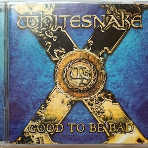May include: A CD case with a blue and gold background. The band Whitesnake is printed in gold letters at the top of the case. The album title "Good to Be Bad" is printed in gold letters at the bottom of the case.