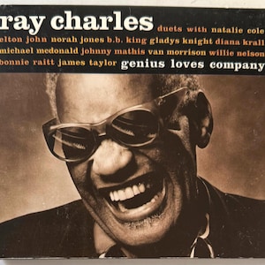 May include: A black and white photo of Ray Charles, wearing sunglasses, smiling and looking to the right. The album cover text reads "ray charles duets with natalie cole elton john norah jones b.b. king gladys knight diana krall michael mcdonald johnny mathis van morrison willie nelson bonnie raitt james taylor genius loves company"