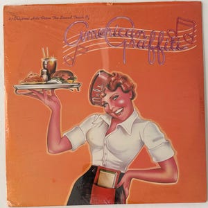 May include: A vintage record album cover featuring a smiling waitress in a red and white uniform holding a tray of food. The album cover is orange with the text "41 Original Hits From The Sound Track Of American Graffiti" and a musical note.