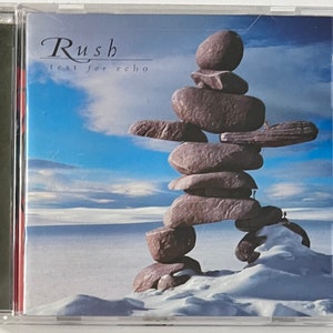 May include: A CD case with a blue sky and white clouds in the background. A stone sculpture is in the foreground. The CD case has the text "Rush Test for Echo" on the front.