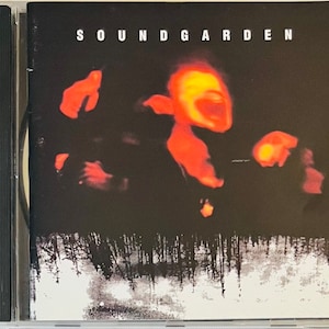 May include: A CD case with a black background and a red and orange image of a person singing. The text "SOUNDGARDEN" is printed in white at the top of the case.
