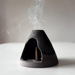 May include: Black ceramic incense burner shaped like a volcano with smoke rising from the top. The burner has a small opening at the top for incense cones.