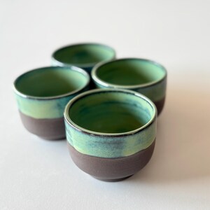 May include: Set of four small ceramic bowls with a green and brown glaze. The bowls are stacked on top of each other.