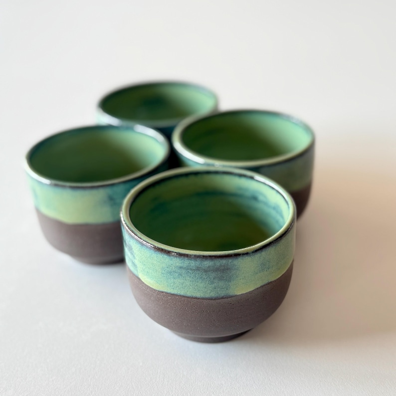 May include: Set of four small ceramic bowls with a green and brown glaze. The bowls are stacked on top of each other.