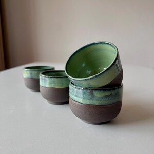 May include: Four small ceramic cups with a green and brown glaze. The cups are stacked on top of each other.