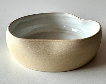 May include: A large, off-white ceramic bowl with a slightly irregular, wavy rim. The bowl has a matte finish and a smooth, white interior.