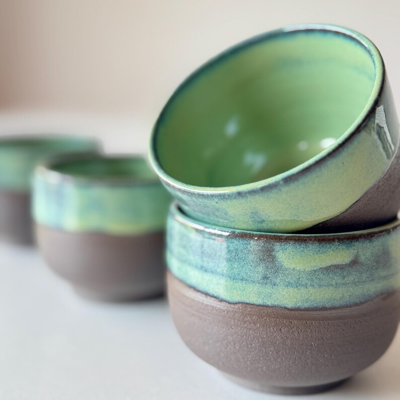 May include: Set of four ceramic bowls with a green glaze and a brown base. The bowls are stacked on top of each other.