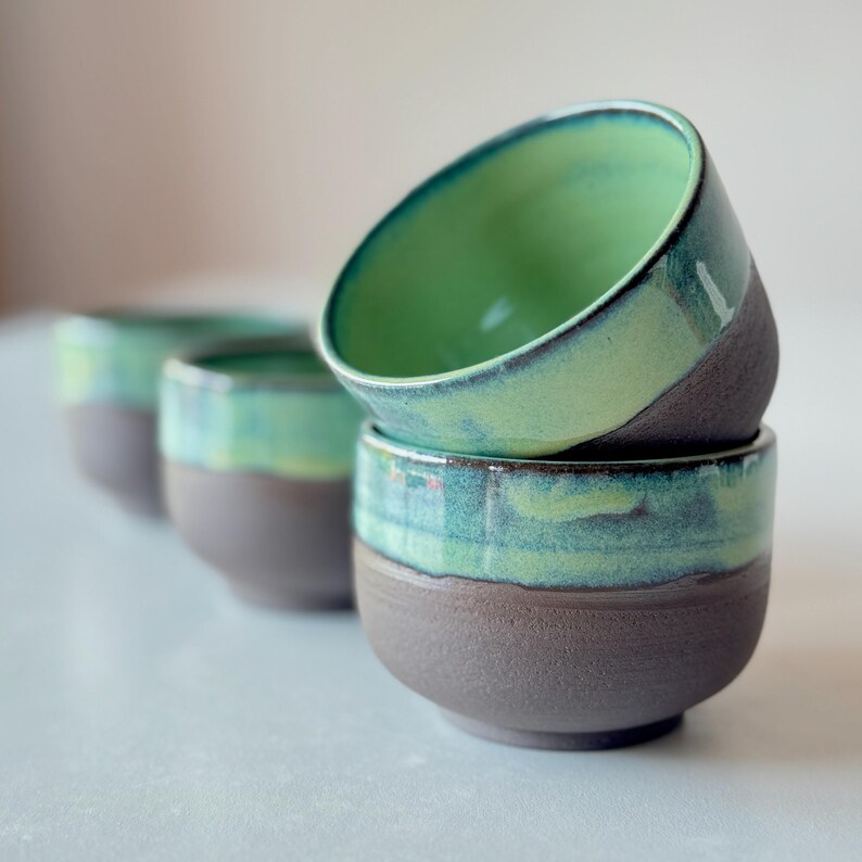 May include: Four ceramic bowls with a green glaze on the inside and a dark brown glaze on the outside. The bowls are stacked on top of each other.