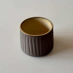 以下が含まれることがあります： 薄い茶色の内側を持つ、濃い茶色の小さなセラミックボウル。ボウルは、テクスチャのあるリブ状の外側を持っています。