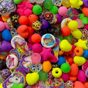 May include: A collection of colorful craft beads in various shapes including stars, hearts, and round spheres. The assortment features translucent and opaque finishes with printed designs of unicorns, octopuses, crabs, and leopard patterns in bright neon and pastel hues.