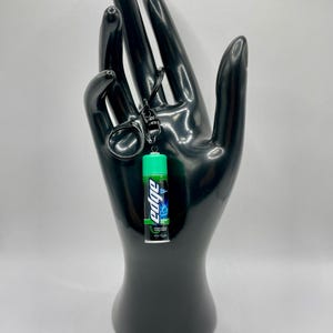 Könnte beinhalten: Ein grüner und blauer Edge-Rasierschaum-Schlüsselanhänger. Der Schlüsselanhänger ist an einem schwarzen Metallring befestigt.