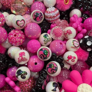 Peut inclure: Un assortiment de perles roses et blanches de différentes tailles et textures. Certaines perles présentent le logo Barbie, des cœurs et d'autres motifs. L'assortiment comprend des perles lisses, texturées et scintillantes, ainsi qu'une grande fleur rose.