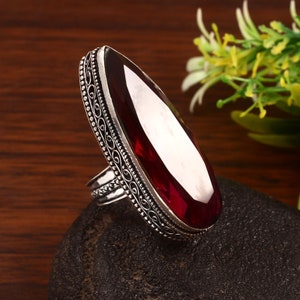 May include: A silver ring with an ornate design and a large, oval-shaped, dark red gemstone.