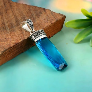 Op de afbeelding: Een zilveren hanger met een versierd ontwerp en een grote, gefacetteerde, blauwe edelsteen.