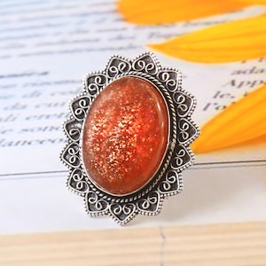 Op de afbeelding: Een zilveren ring met een ovale zonnesteen. De ring heeft een gedetailleerd, sierlijk ontwerp met een zilveren filigraanpatroon.