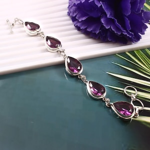 Puede incluir: Una pulsera de plata con cinco piedras preciosas de amatista en forma de lágrima. La pulsera tiene un cierre de langosta.