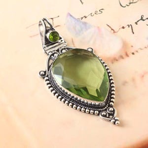 May include: A silver pendant with a large, faceted, green gemstone. The pendant has a detailed, ornate design with small beads around the edge.