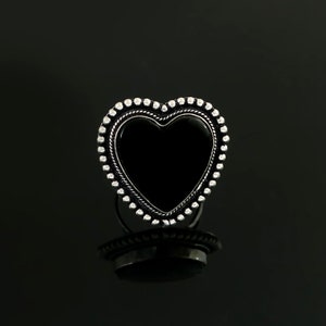 May include: A silver heart-shaped ring with a black onyx stone in the centre. The ring is decorated with a beaded border.