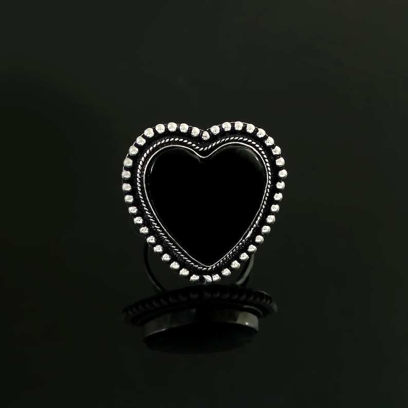 May include: A silver heart-shaped ring with a black onyx stone in the centre. The ring is decorated with a beaded border.