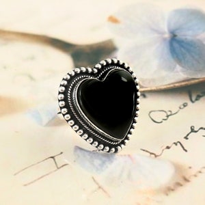 May include: A silver ring featuring a black heart-shaped gemstone. The ring has a beaded border around the gemstone.