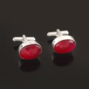 May include: A pair of silver cufflinks with red gemstone accents. The cufflinks are oval shaped and have a polished finish.