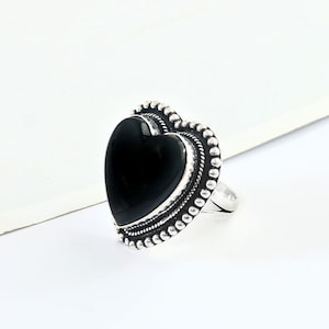 May include: A silver ring featuring a black heart-shaped stone. The ring has a beaded design around the stone.