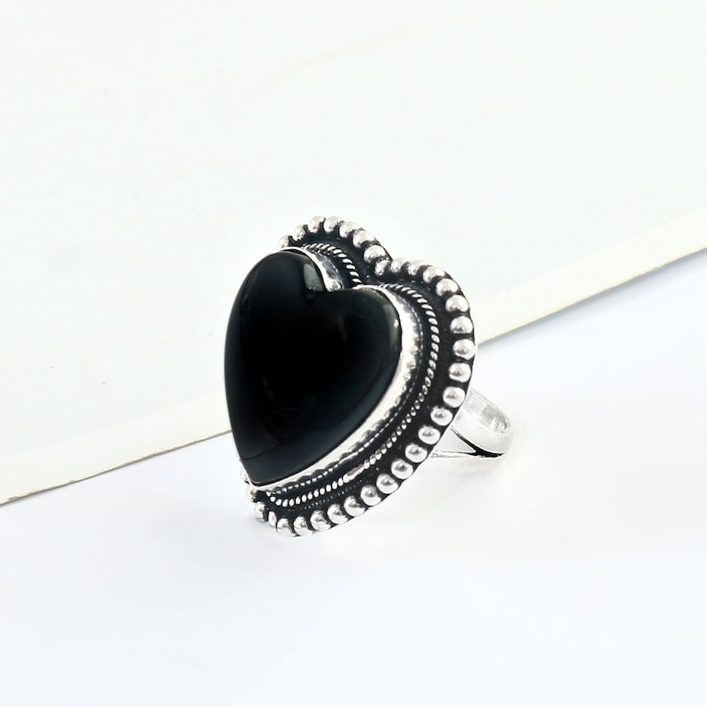 May include: A silver ring featuring a black heart-shaped stone. The ring has a beaded design around the stone.