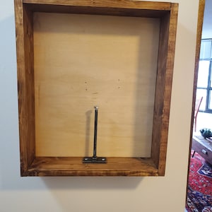 May include: A wooden frame with a plywood back and a metal rod attached to the bottom. The frame is stained a dark brown color.