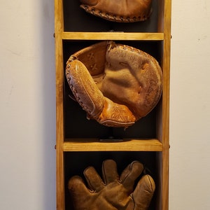 May include: Three vintage baseball mitts displayed in a wooden shadow box. The mitts are brown leather with white stitching. The top mitt has no markings. The middle mitt has the text "Twin Action" and "Rawlings" on it. The bottom mitt has no markings.