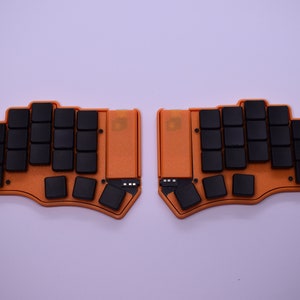 Può includere: Due metà di tastiera separate di colore arancione e nero con tasti neri e una superficie testurizzata.