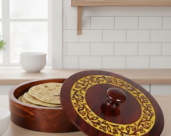 May include: A wooden tortilla warmer with a decorative lid, featuring a dark brown finish and a yellow floral design. The warmer is open, revealing a stack of tortillas. A white bowl sits nearby.