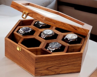 May include: A wooden watch box with a hinged lid and a clear glass top. The box has a honeycomb design with six compartments for storing watches. The box is made of dark wood with a natural finish.
